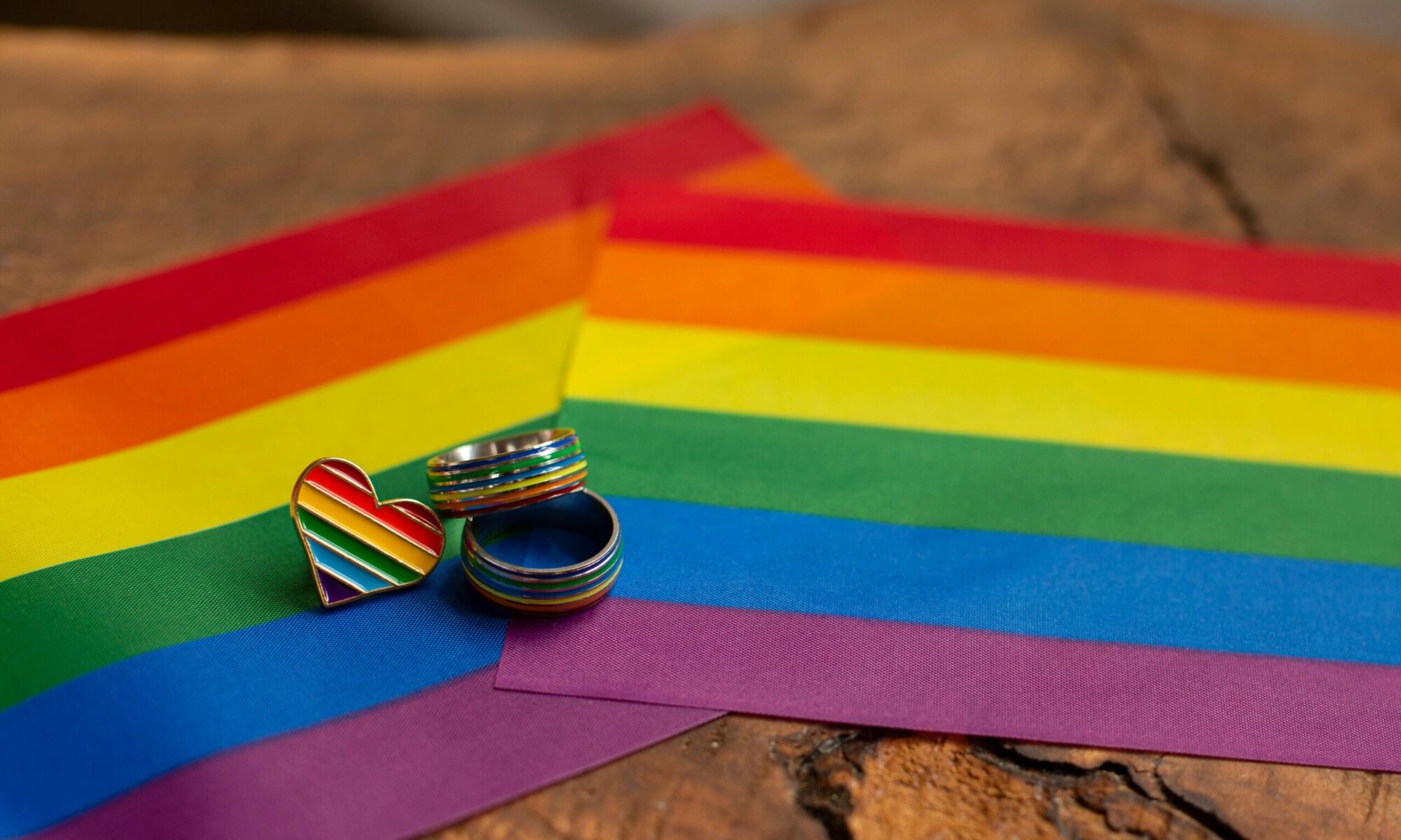Close-up of rainbow rings and heart pin on a pride flag, symbolic of LGBTQ pride and love.